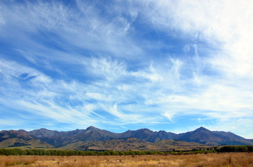 Fototapeta na wymiar Wispy clouds in blue skies above a rugged mountain range in New Zealand