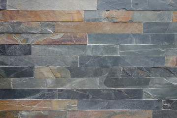 Roughly textured stone cladding tiled wall in grey and ochre colours background