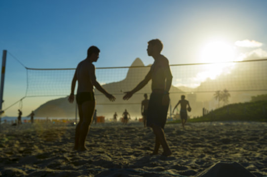 Defocus view of silhouettes of Brazilians shaking hands on a beach volleyball court in Rio de Janeiro, Brazil at sunset on Ipanema Beach