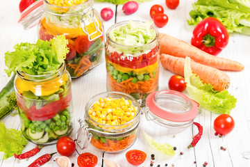 Colorful vegetables in glass jars on wooden background.