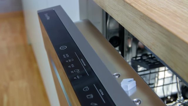 A young lady is trying out and pressing all the buttons on a dishwasher. She needs to adjust the settings before using it.
