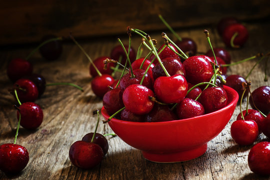 Red sweet cherry in a red bowl , dark vintage wooden background,