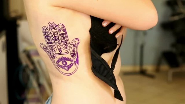 Girl stands in the studio of tattoo with finished tattoo
