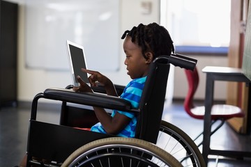 Schoolboy sitting on wheelchair and using digital tablet
