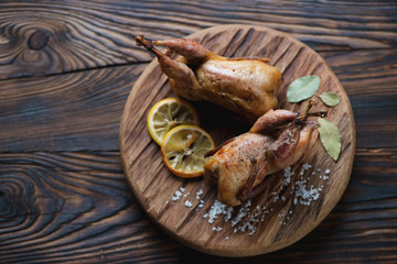 Serving board with whole baked quails in a rustic wooden setting