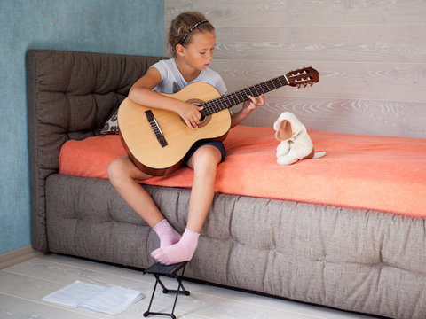 Little girl sitting on the bed in the room, and learning to play a musical instrument