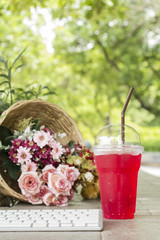 Red beverage with soda water in plastic glass, flowers basket an