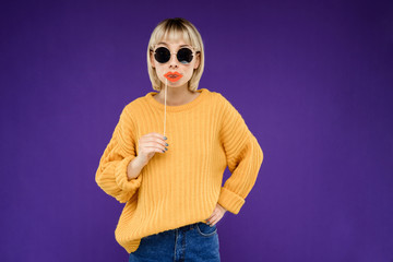 Portrait of young girl wearing fake lips over purple background.