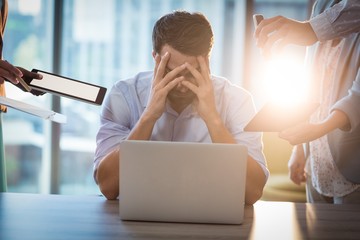Frustrated businessman sitting on desk with hand on head