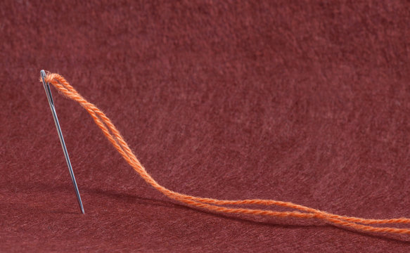 Needle anb Thread of  Yarn on the Red Felt Fabric Background Te