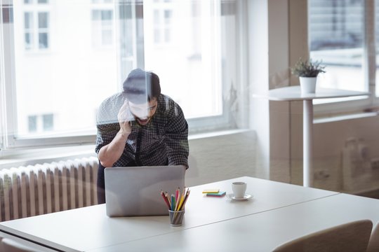 Editor talking on mobile phone while using laptop 