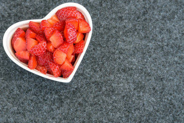 Diced strawberries in a white heart shaped bowl on a black background 
