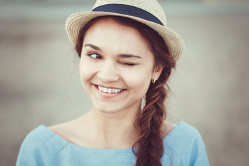 Closeup portrait of funny beautiful smiling white Caucasian brunette girl winking, in blue dress and straw hat, rustic country retro vintage style concept