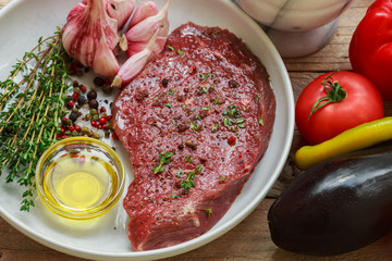 Raw beef with spices and thyme and fresh vegetables on the table - peppers, tomatoes, eggplant, garlic. The ingredients for the warm salad

