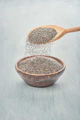 Chia Samen fallen in eine Holzschüssel auf blau weißen Untergrund