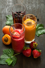 Fresh strawberry, blueberry and apricot smoothies on black wooden background. Selective focus