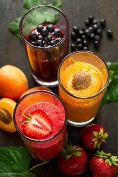 Fresh strawberry, blueberry and apricot smoothies on black wooden background. Selective focus
