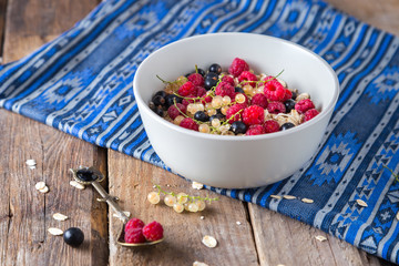 Healthy breakfast, oatmeal with currant and raspberries in a bowl on a wooden background   and blue napkin 