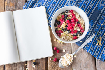 Healthy breakfast, oatmeal with currant and raspberries on a wooden background and an opened notebook nearby, top view 