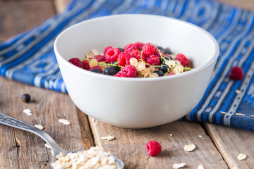 Healthy breakfast, oatmeal with currant and raspberries in a bowl on a wooden background   and blue napkin 