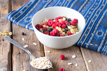Healthy breakfast, oatmeal with currant and raspberries in a bowl on a wooden background   and blue napkin 