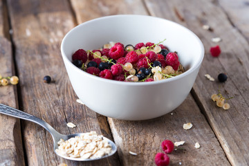 Healthy breakfast, oatmeal with currant and raspberries in a bowl on a wooden background 