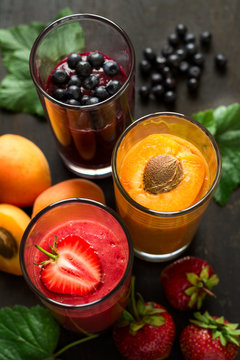Fresh strawberry, blueberry and apricot smoothies on black wooden background. Selective focus