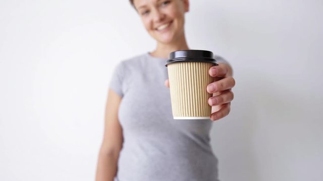 Unfocused handsome girl in blank shirt shows unlabeled brown paper cup on camera smiling