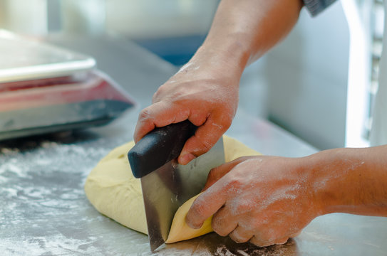 Bakers hands working and cuttting bread dough on metal surface with flour spread out