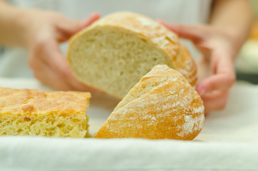 Bakers hands placing half cut loaf of bread onto white plate next to other breads