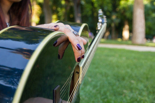 Girl playing guitar in the park in summer. She is sitting on the grass. 