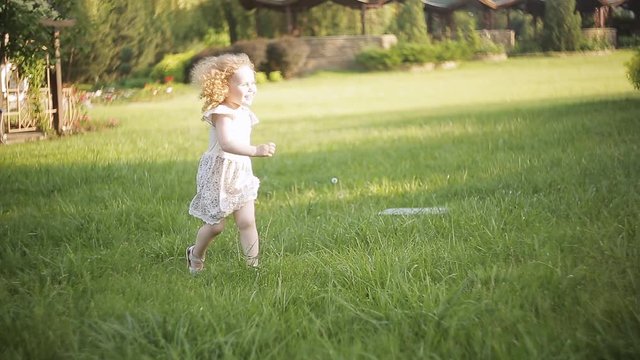 happy little child girl running on on green meadow field to her mother