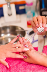 Obraz na płótnie Canvas Closeup females hands getting manicure treatment from woman applying transparent liquid in salon environment, pink towel surface, blurry background products