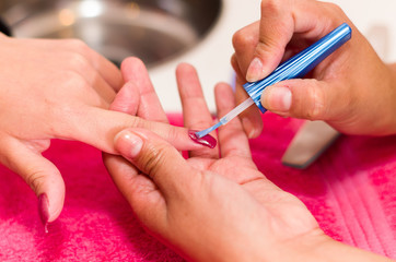 Closeup females hands getting manicure treatment from woman using small brush in salon environment, pink towel surface, blurry background products