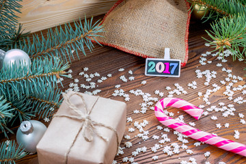 Fototapeta na wymiar christmas gifts packaged in craft paper and black nameplate with colorful wood new year numbers, pink candy cane, sprinkling as snowflakes on wooden table.