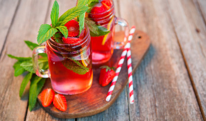 Red lemonade with strawberries and mint on an old wooden table i