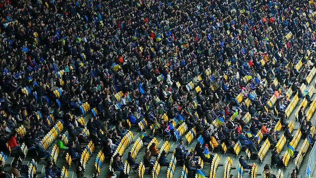 Great number of people sitting on tribunes and watching football game, stadium