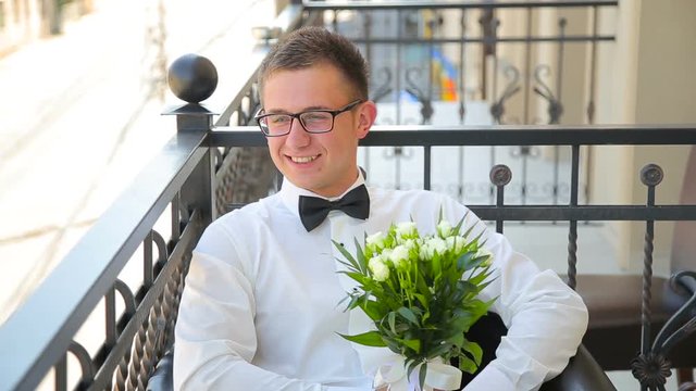 Young man is sitting with wedding bouquet on the balcony