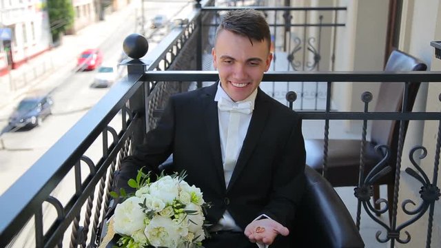 Groom with wedding bouquet and rings sitting on a balcony and smiling