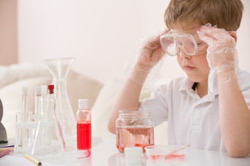 Cute kid boy in glasses making science experiments. Little child working with liquids.