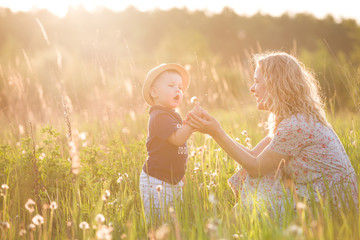 Cute little toddler boy in a straw hat holding his mother's hand and blowing dandelion. Adorable...