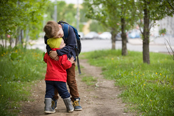 Fototapeta premium Two little brothers hugging each other when meeting in the park. Cute kid boy meets his little toddler sibling and hugs him. Happy children walking on the road. Lifestyle and family concept