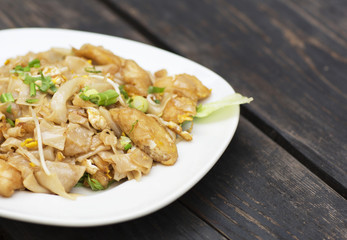Thai food for lunch in a plate on a wooden table. Fried noodles with fish, egg and greens. 