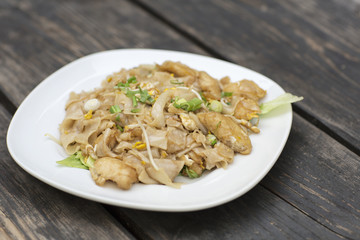 Thai food for lunch in a plate on a wooden table. Fried noodles with fish, egg and greens. 
