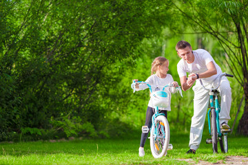 Young father and little girl biking at summer warm day. Young active family ride on bicycles