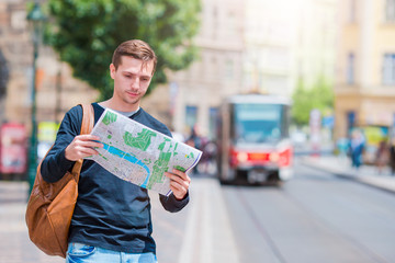 Young man in sunglasses with a city map and backpack in Europe. Caucasian tourist looking at the map of European city in search of attractions.
