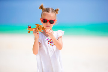 Happy little girl with toy airplane in hands on white sandy beach. Photo travel advertising, flights and airlines