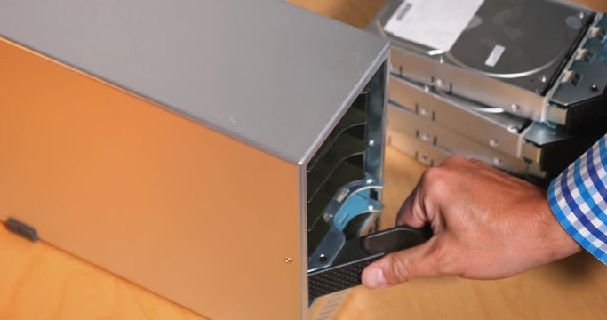 An IT computer technician inserts five hard drives into an external desktop RAID array.  	
