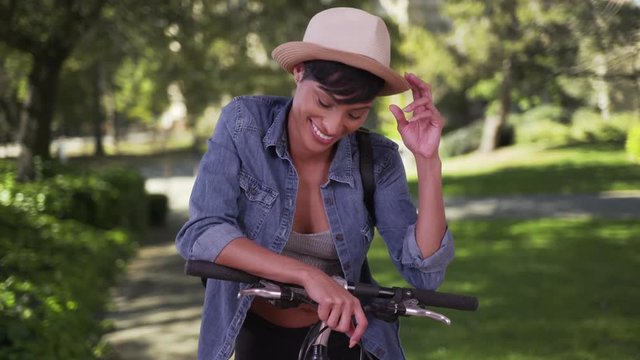 Happy smiling black woman leaning against handlebars on bike in park