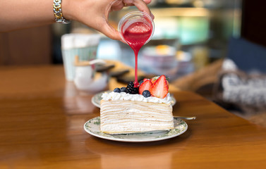 Hand pouring strawberry sauce over crape cake